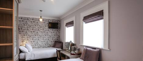 A bedroom with two beds, a desk, a television, and a brick-patterned wall.