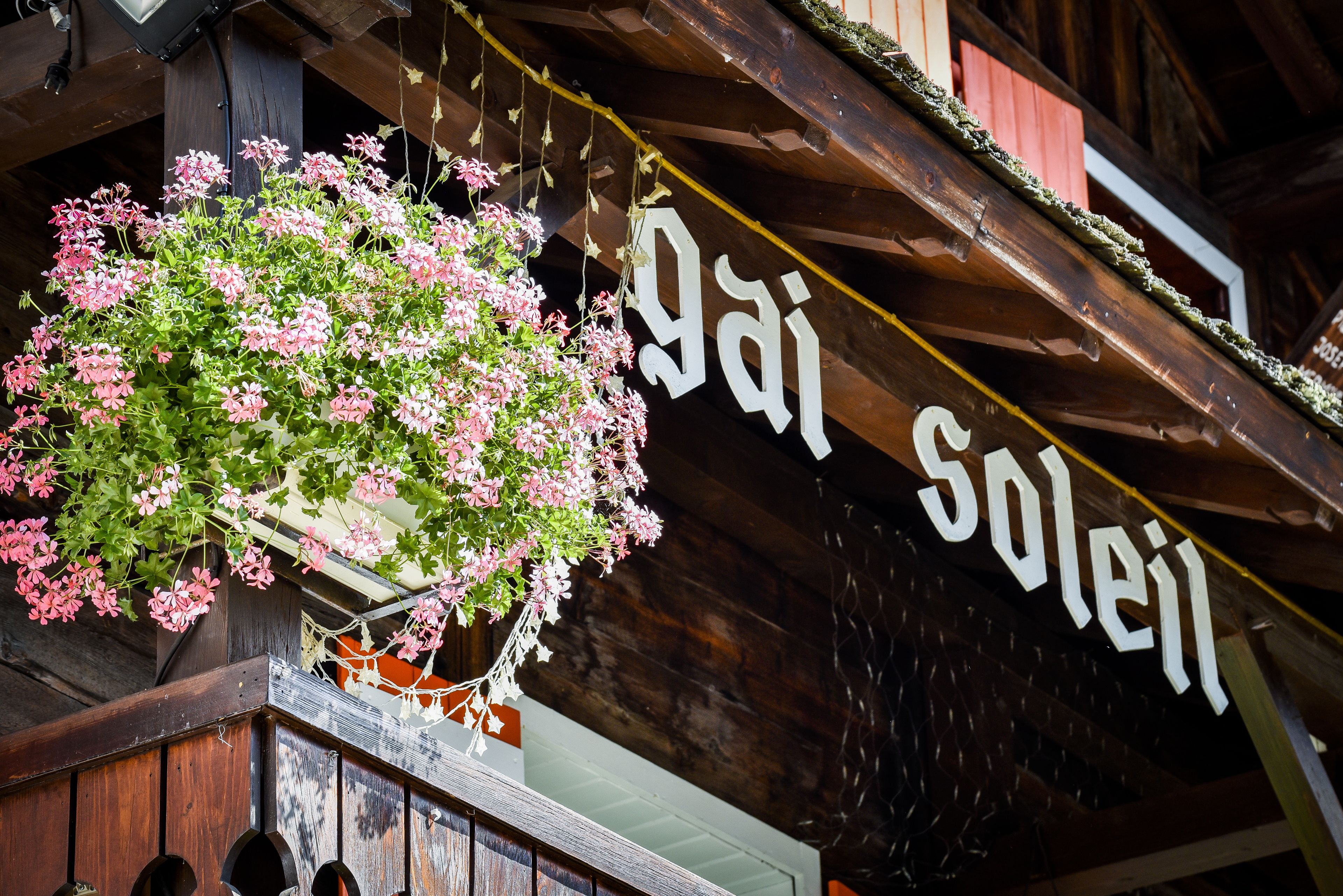A wooden building with a hanging flower basket and a sign that reads "gai soleil".