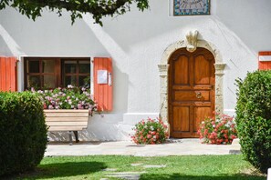 Ein Gebäude mit einer Holztür, einem Fenster mit Fensterläden und einer Bank mit Blumen.