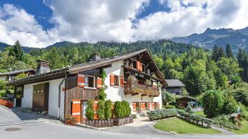 Situated in a mountainous area, this chalet-style building offers a traditional Alpine design with a sloped roof and wooden balconies.