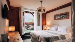 Un dormitorio con cama, lámparas de noche, un escritorio de madera, una silla, una ventana con vistas y una puerta que da a un balcón.