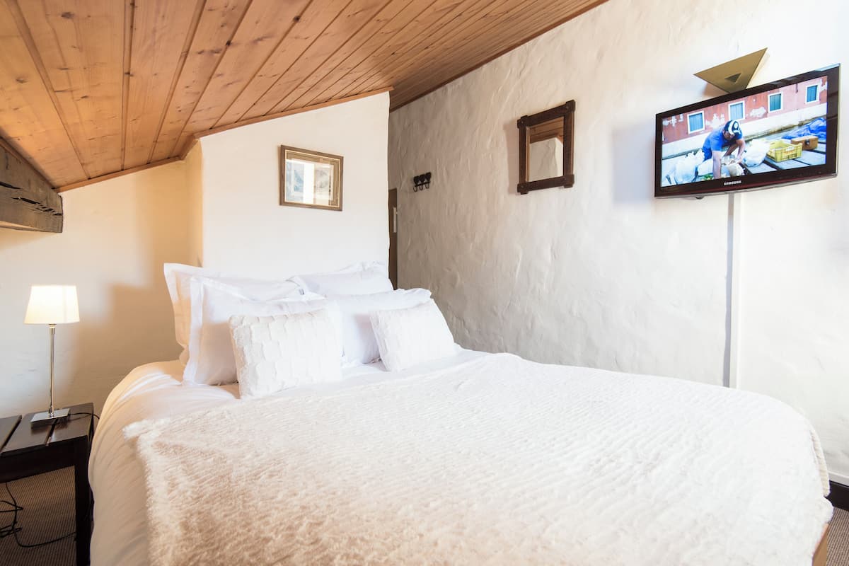 A hotel room with a large bed, a television on the wall, and a lamp on a bedside table.