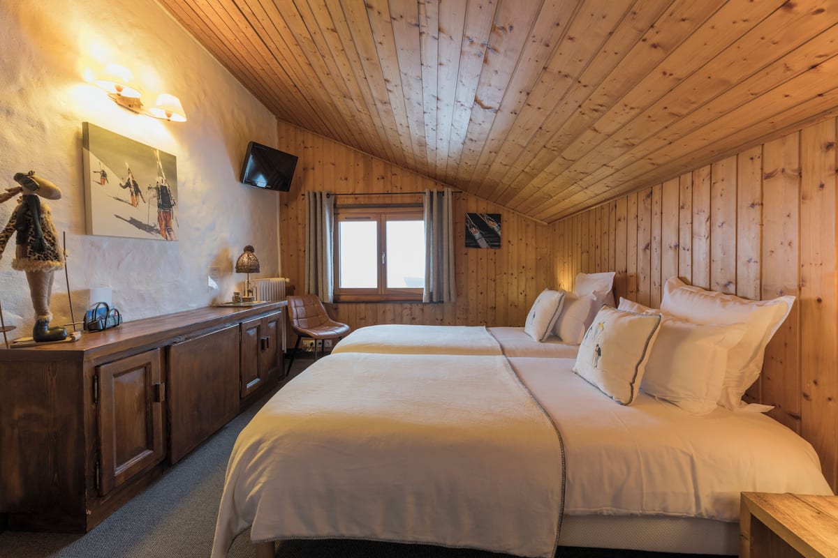 A wooden-paneled room with a bed, a desk, a chair, and a television mounted on the wall.