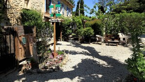 A courtyard with a stone building, a wooden fence, and a signpost with directions. - Mas Saint Antoine (Rognonas)