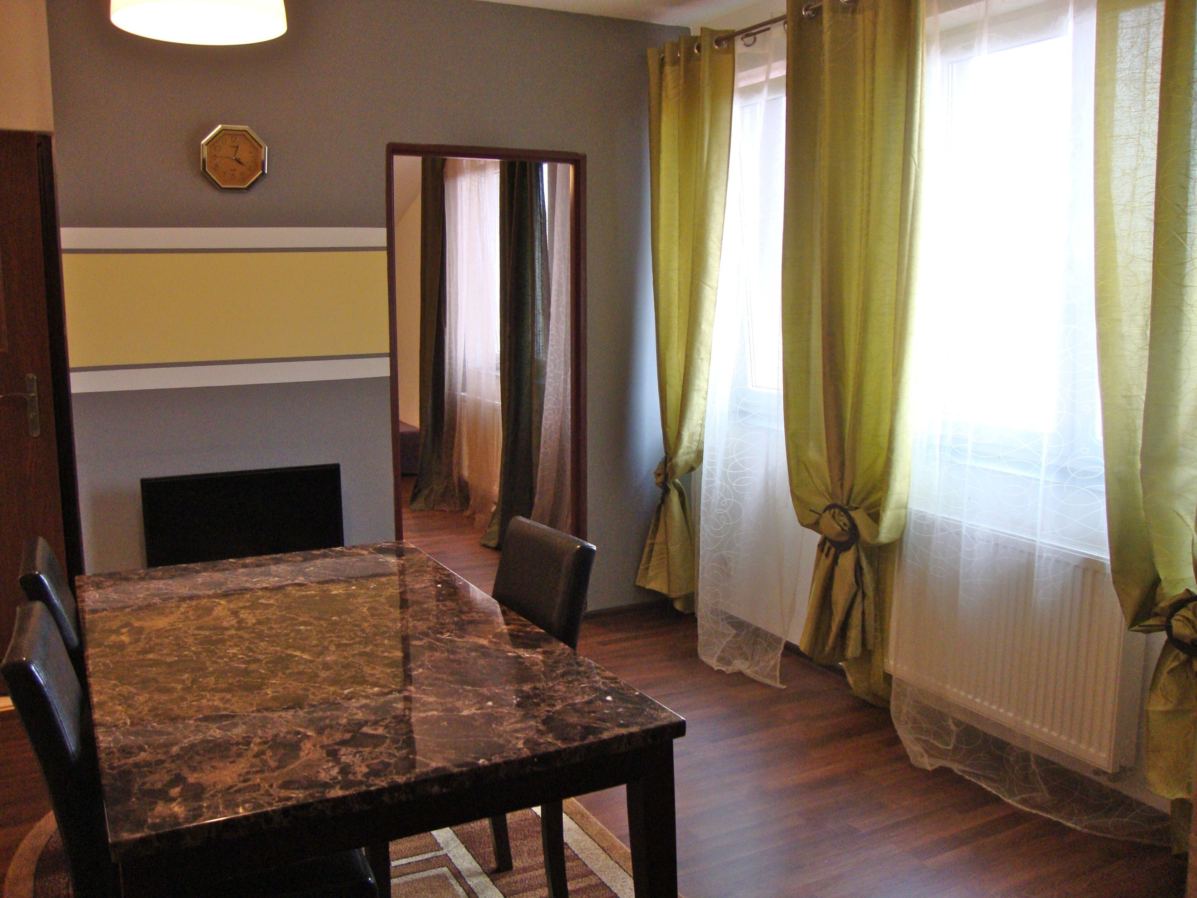 A dining area with a marble table and chairs, a clock on the wall, and curtains on the windows.
