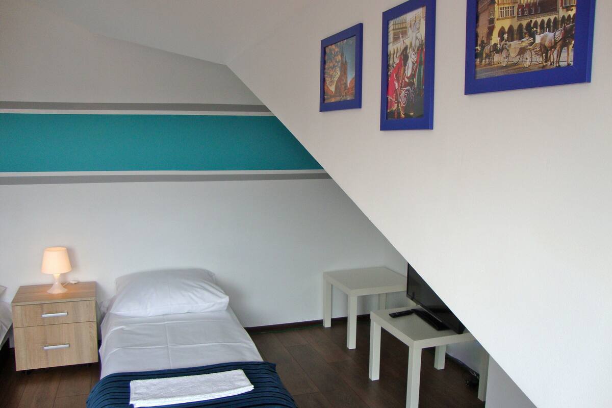Een slaapkamer met een bed, een nachtkastje, een lamp, een kleine tafel en twee ingelijste foto's aan de muur.