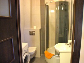Une petite salle de bain comprenant des toilettes, un lave-linge, une douche à parois de verre et un lavabo.