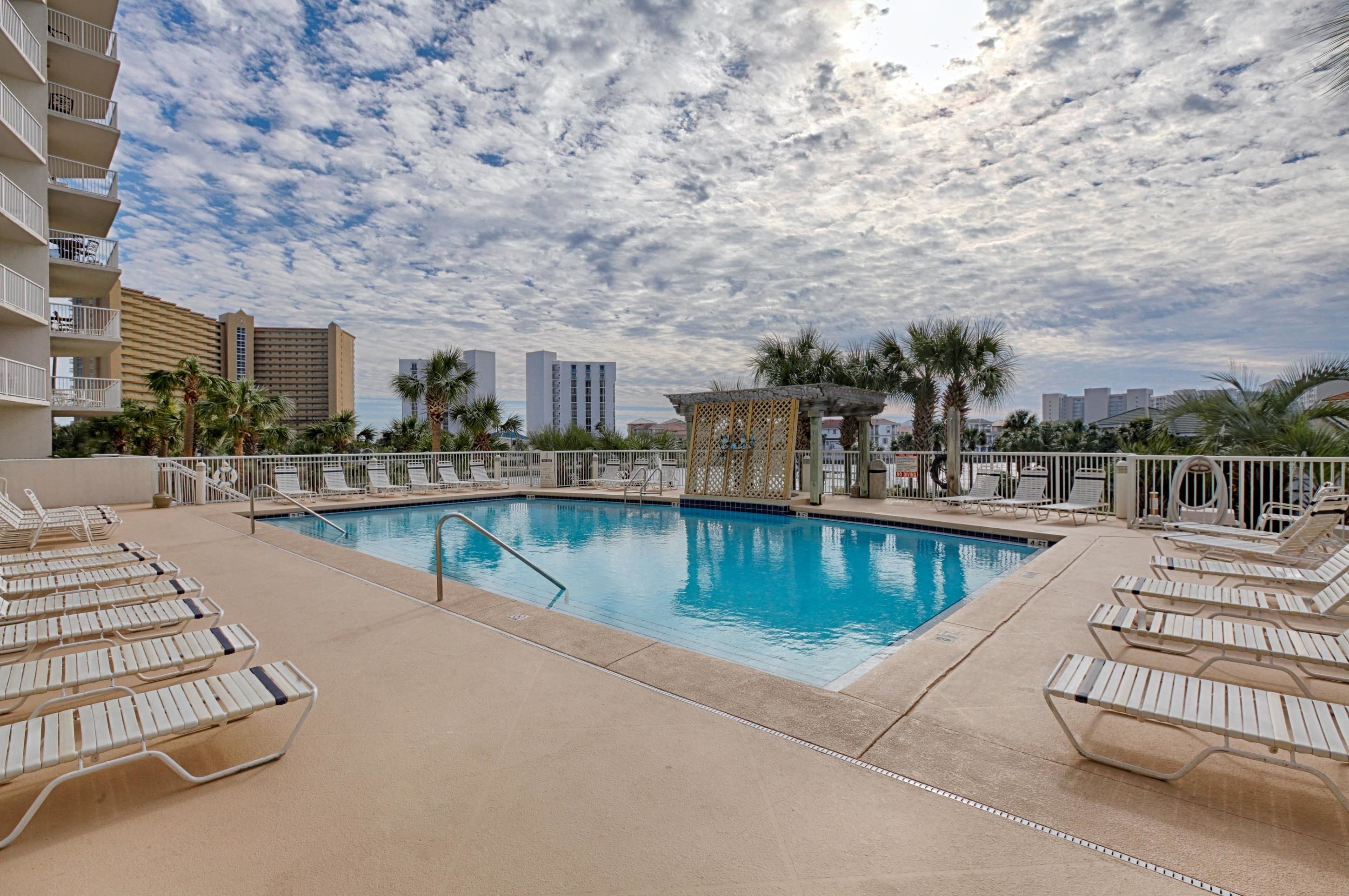 A swimming pool with lounge chairs, palm trees, and a city skyline in the background.