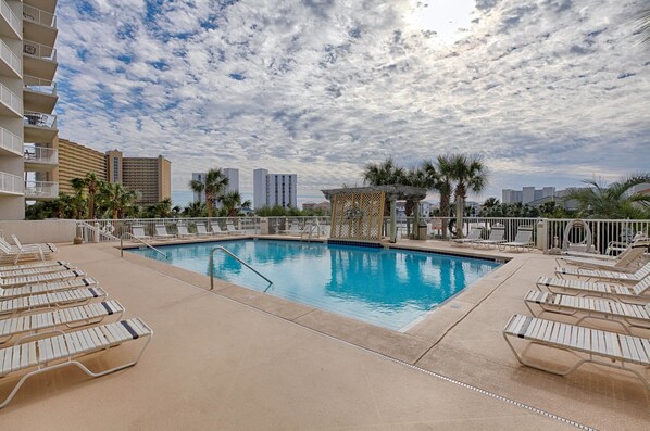 A swimming pool with lounge chairs, palm trees, and a city skyline in the background.