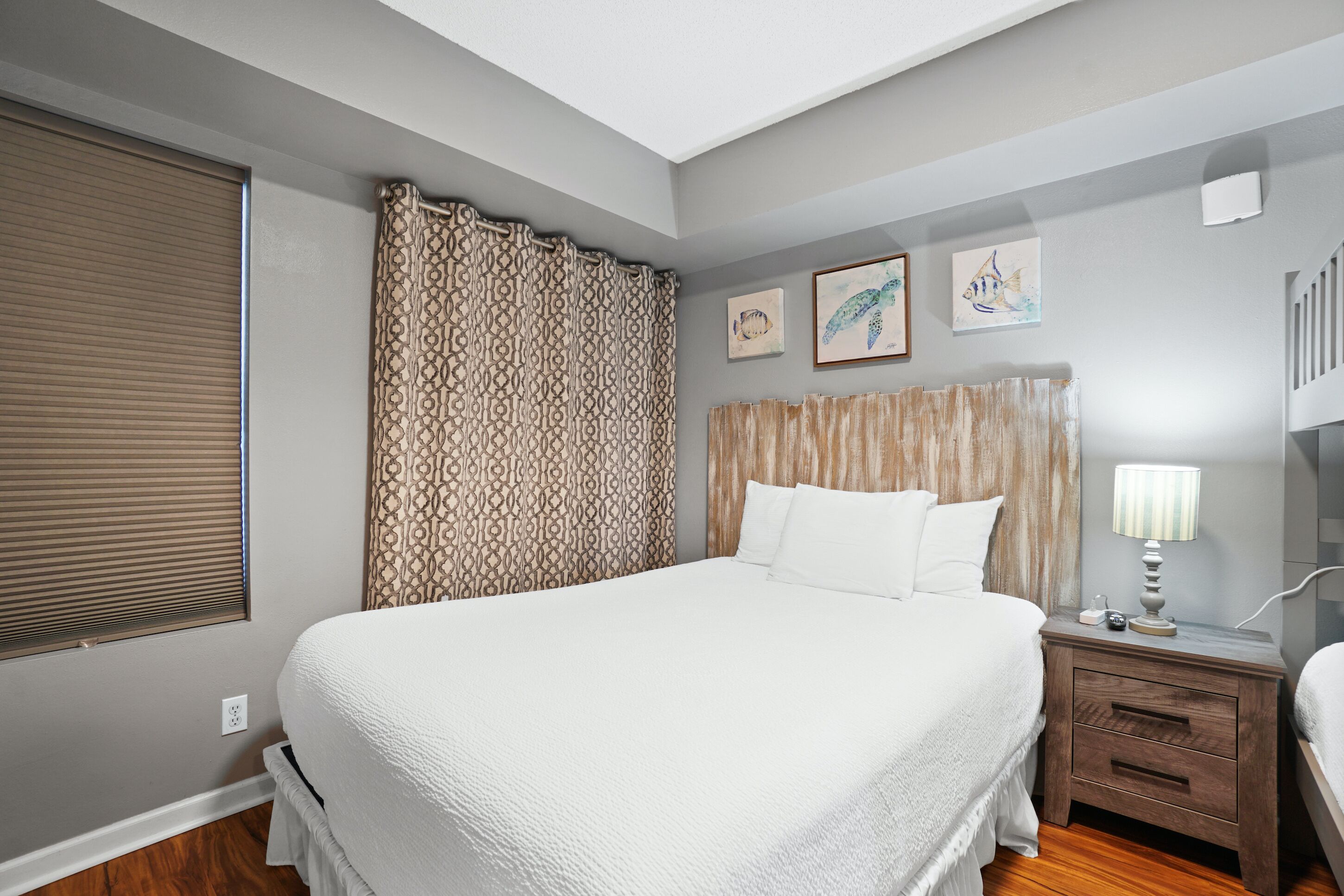 Une chambre à coucher avec un grand lit, une tête de lit en bois, une table de chevet avec une lampe et une fenêtre avec des stores.