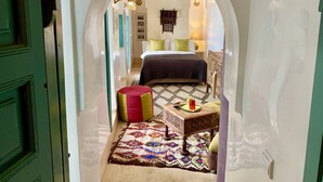A narrow hallway leading to a bedroom with a bed, a small table, a colorful rug, and a green door. - Riad 11 Zitoune (Marrakech)