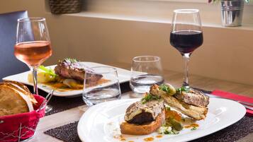 A dining table with plates of food, glasses of wine, and a basket of bread.