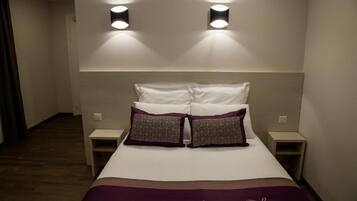 A neatly made bed with two pillows, two bedside tables, and two wall-mounted lights.