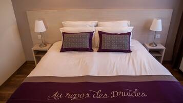 A neatly made bed with a white and purple bedspread, two patterned pillows, and two bedside lamps on matching nightstands.