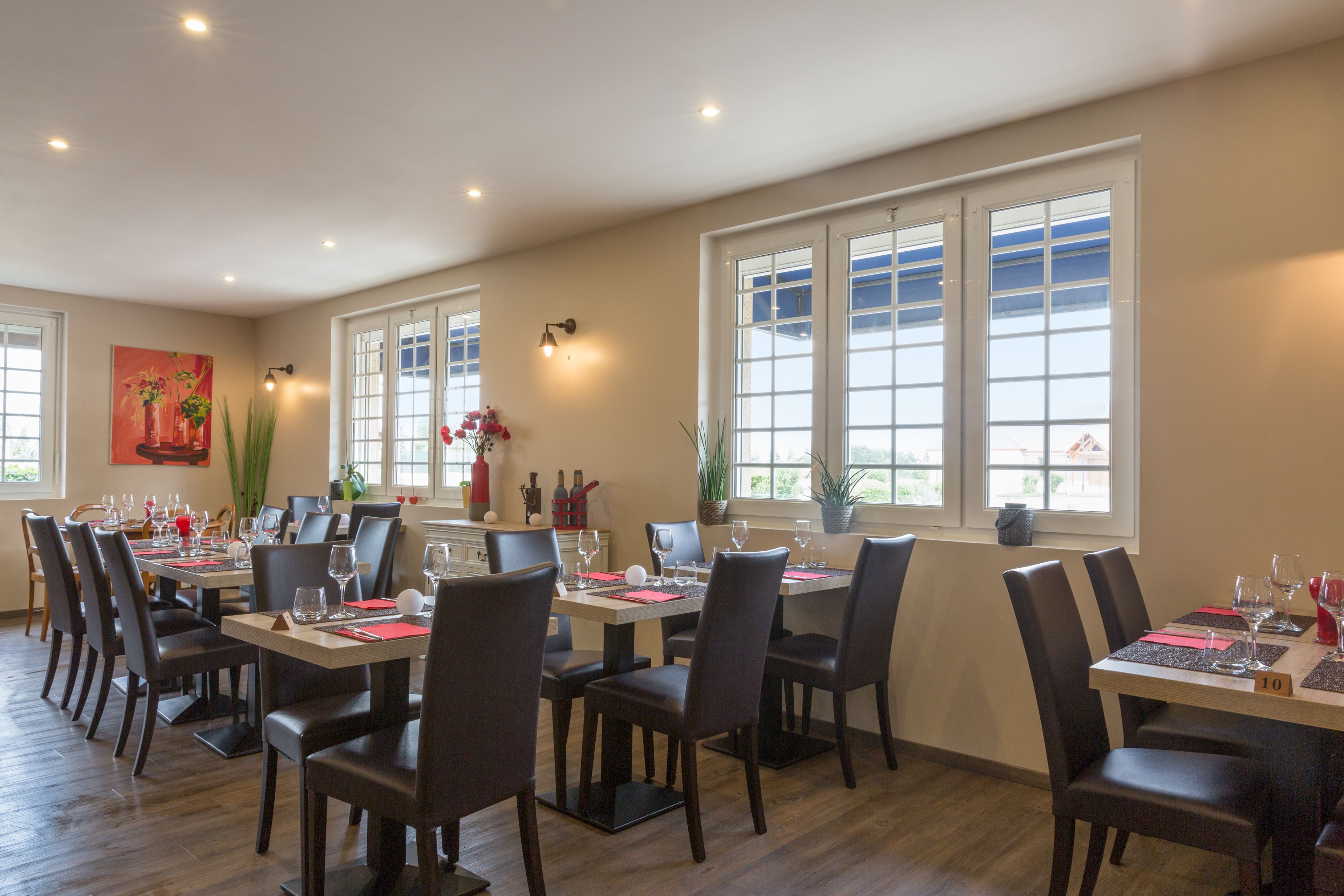 A dining area with multiple tables and chairs, large windows, and decorative plants.