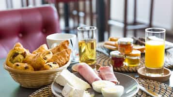 Et morgenbord med bagværk, ost, skinke, æg og drikkevarer på et bord.