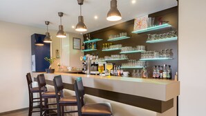 A modern bar area with a counter, bar stools, and shelves stocked with glasses and bottles.