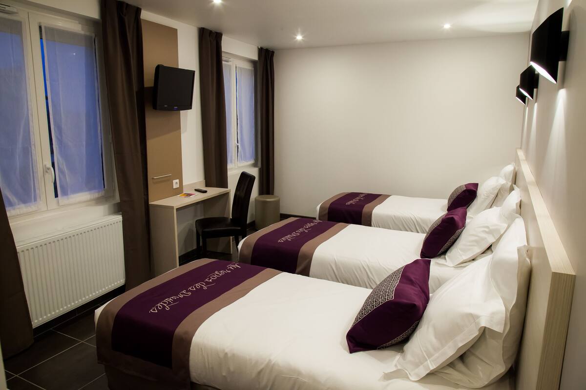 Habitación de hotel con dos camas, un escritorio, una silla, un televisor y una ventana con cortinas.