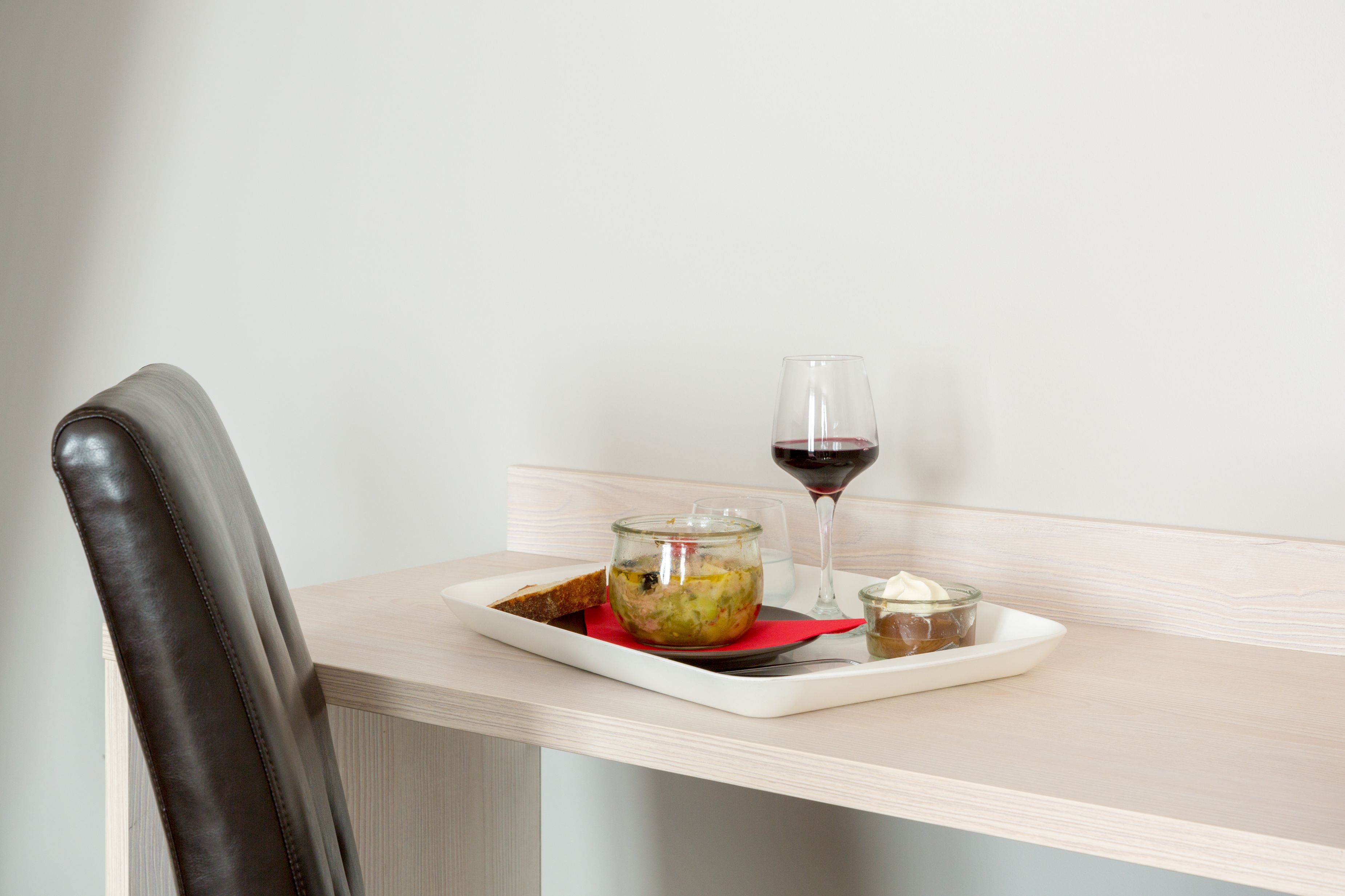 A dining table with a glass of red wine, a jar of food, and a small dish with cream.