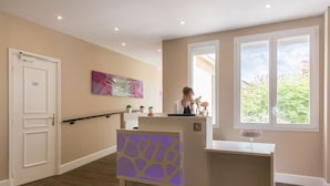 A reception area with a reception desk, a wheelchair-accessible sign, a reception counter, and a window with a view of greenery.