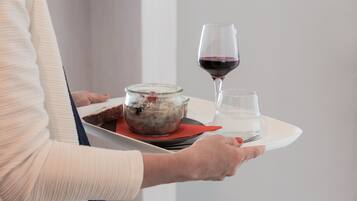 A person holding a tray with a glass of red wine, a glass of water, and a bowl of food.