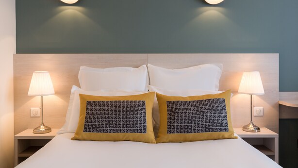 A neatly made bed with white linens and two decorative pillows, flanked by two bedside lamps on matching nightstands.