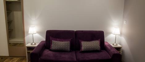 Un sofá morado con almohadones estampados, dos lámparas de noche y un suelo de madera.