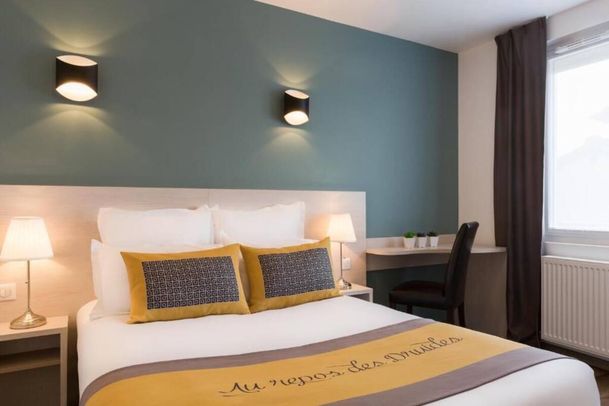 Une chambre d’hôtel avec un lit, deux lampes fixées au mur, un bureau et une chaise.