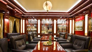 Um quarto luxuoso com uma grande mesa de madeira, cadeiras de couro, um candelabro e uma estante repleta de livros e garrafas.