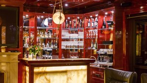 Uma área de bar com balcão de madeira polida, assentos de couro e variedade de garrafas e copos em prateleiras.