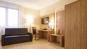 Quarto de hotel moderno com sofá, escrivaninha, televisão e guarda-roupa.