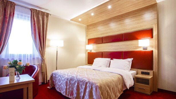 Quarto de hotel com uma cama grande, mesas de cabeceira, escrivaninha com cadeira e janela com cortinas.