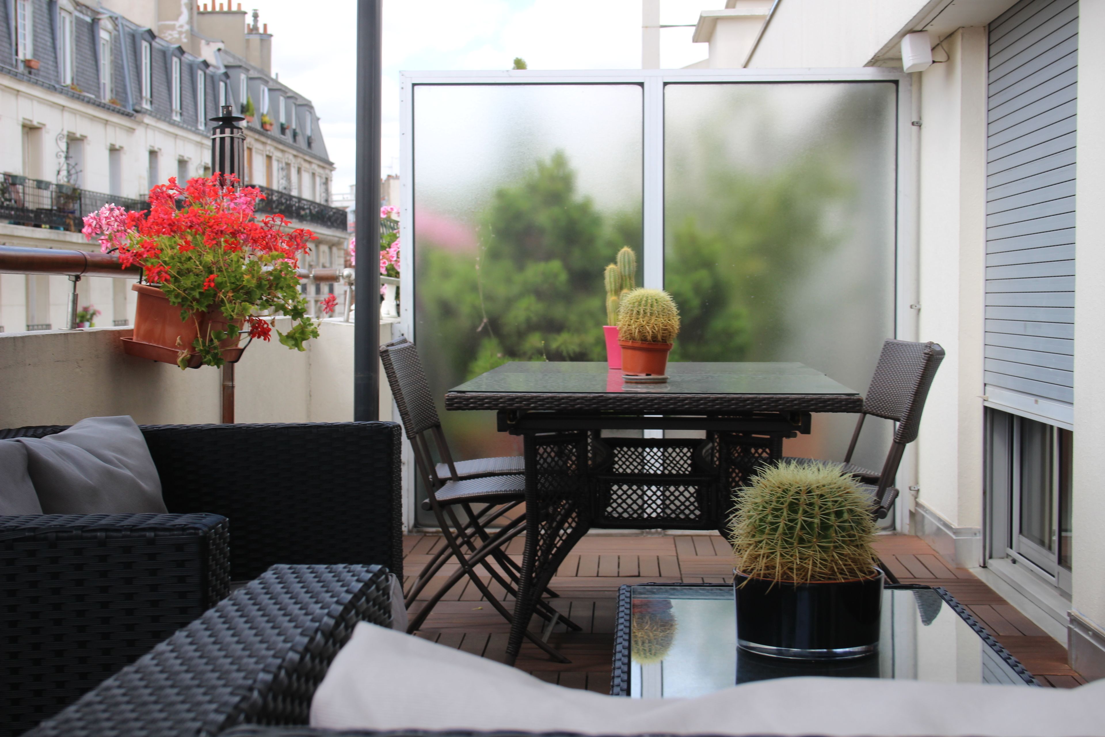 Un balcon agrémenté de meubles en osier, d’une table et de plantes en pot.