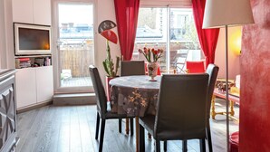 Un comedor con una mesa dispuesta para cuatro, un televisor montado en la pared y una ventana con cortinas rojas.