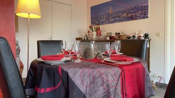 Un coin repas avec deux tables dressées pour le repas, une lampe et un tableau représentant un paysage urbain accroché au mur.