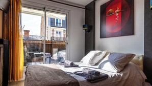 Una habitación de hotel con cama, un ventanal con cortinas, una lámpara de pared y un cuadro.
