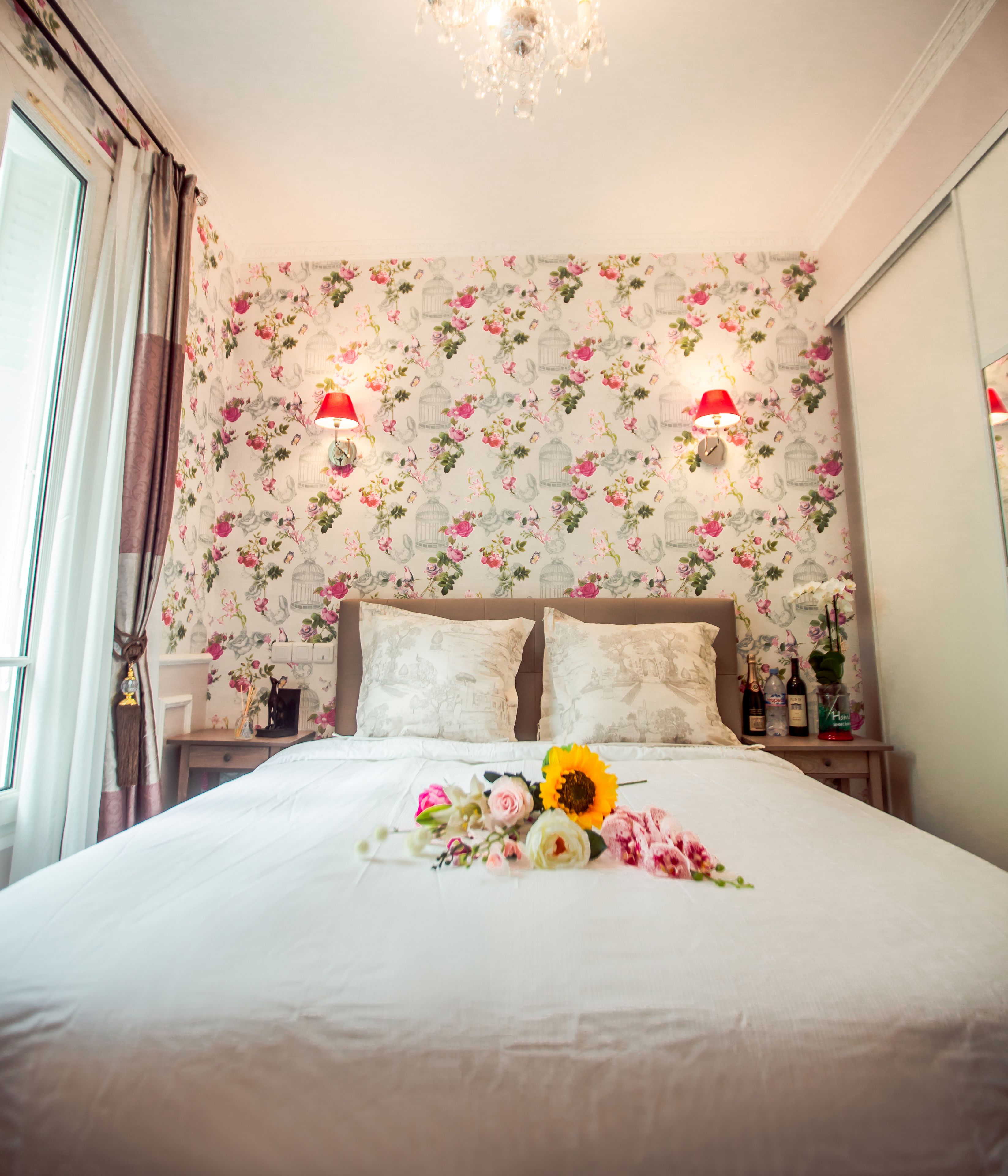 A neatly made bed with floral bedding, two bedside lamps, and a floral arrangement on the bed.