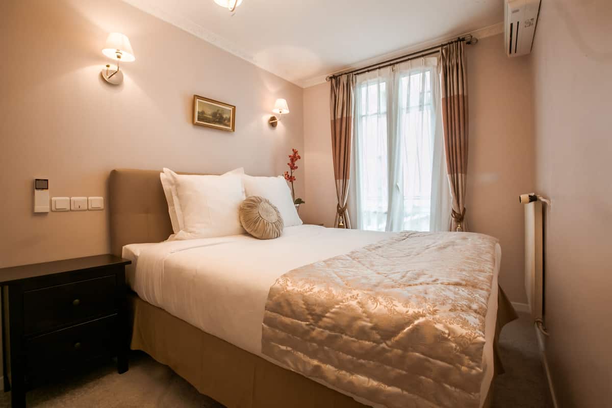 A bedroom with a bed, nightstand, wall-mounted lamp, and a window with curtains.