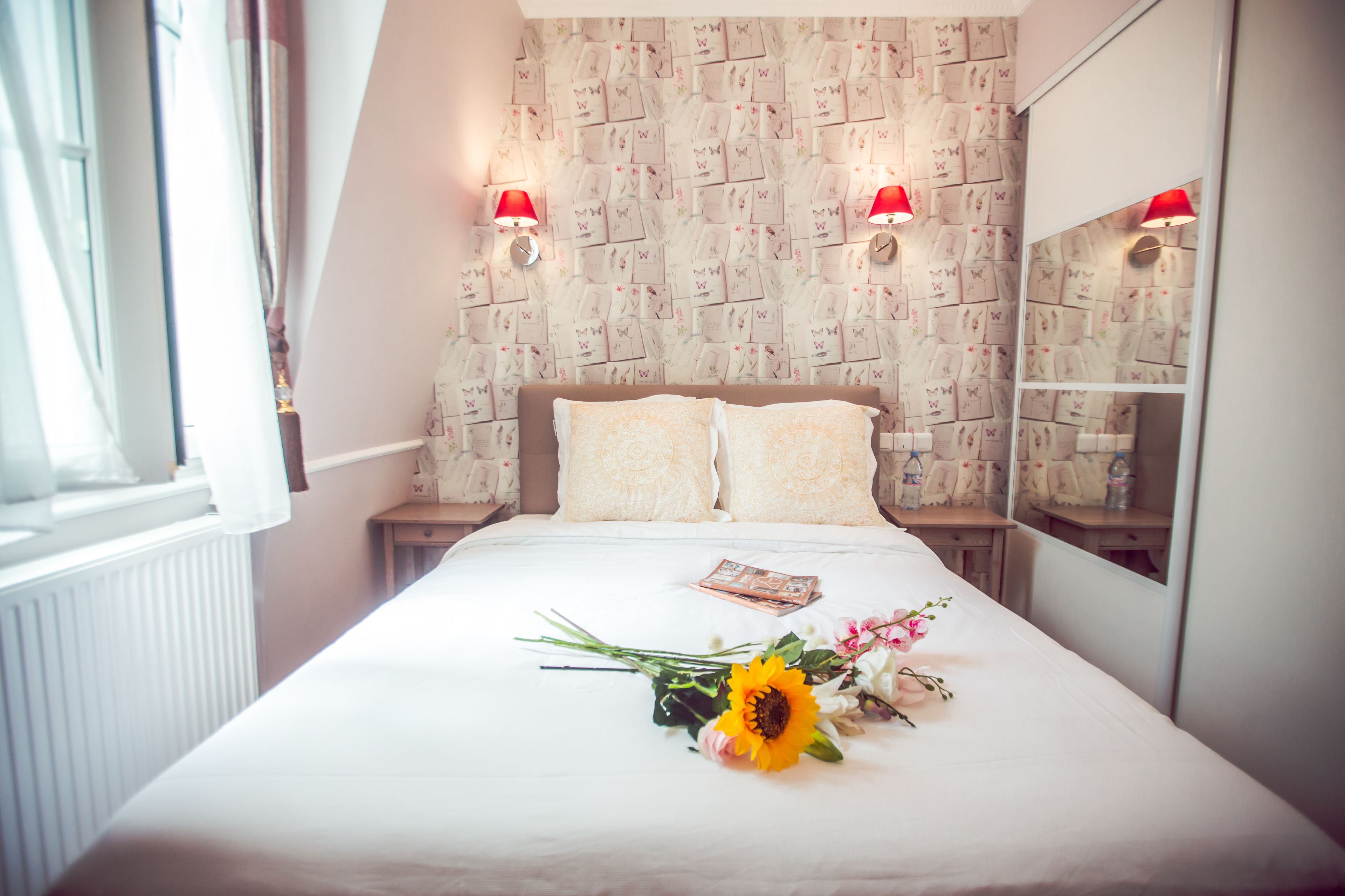 Una cama bien hecha con un ramo de flores, una mesita de noche y un espejo.