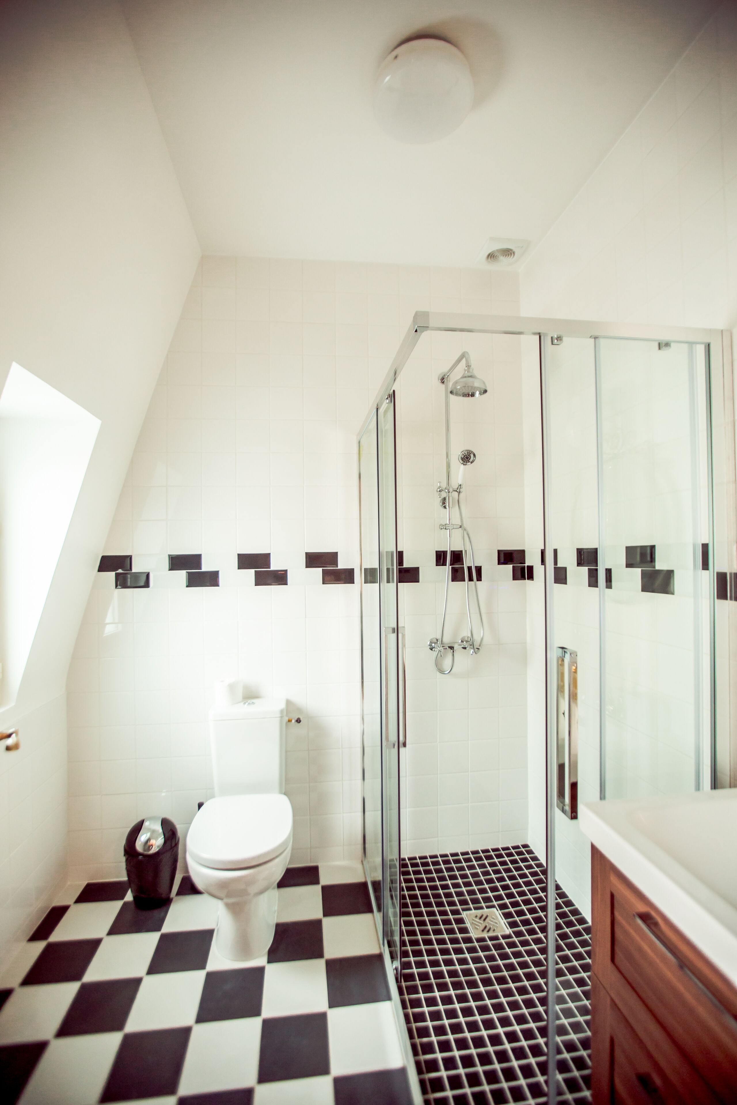 A bathroom with a checkered floor, a glass shower enclosure, a white toilet, and a wooden vanity.