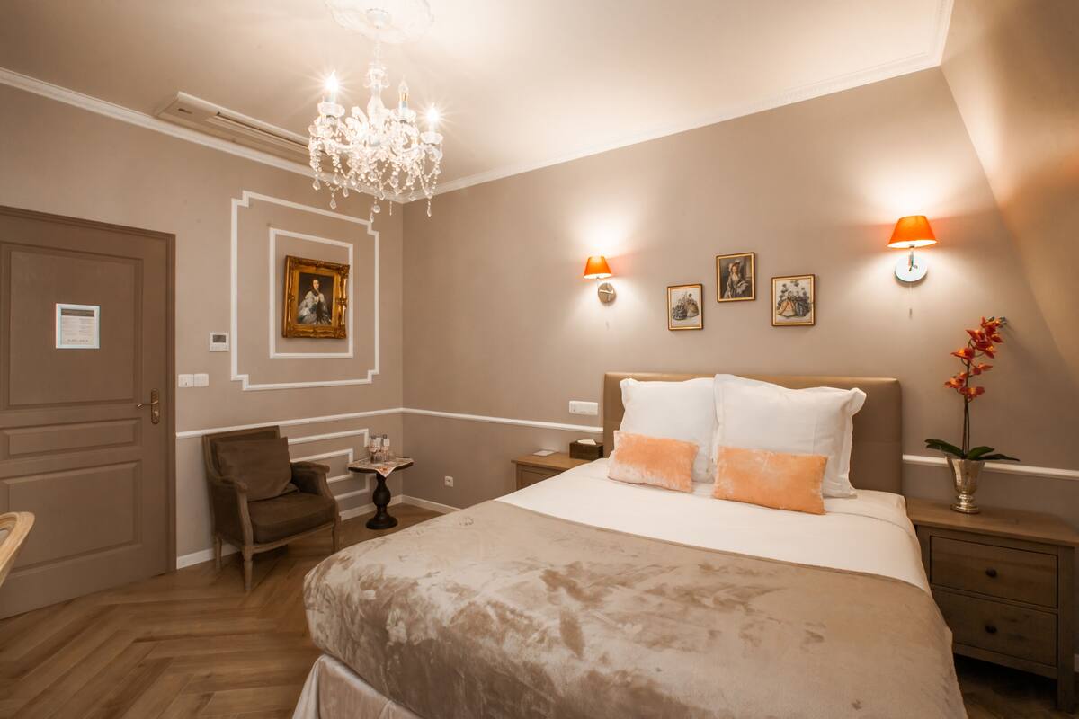 A bedroom with a large bed, a chandelier, a desk, and a chair.