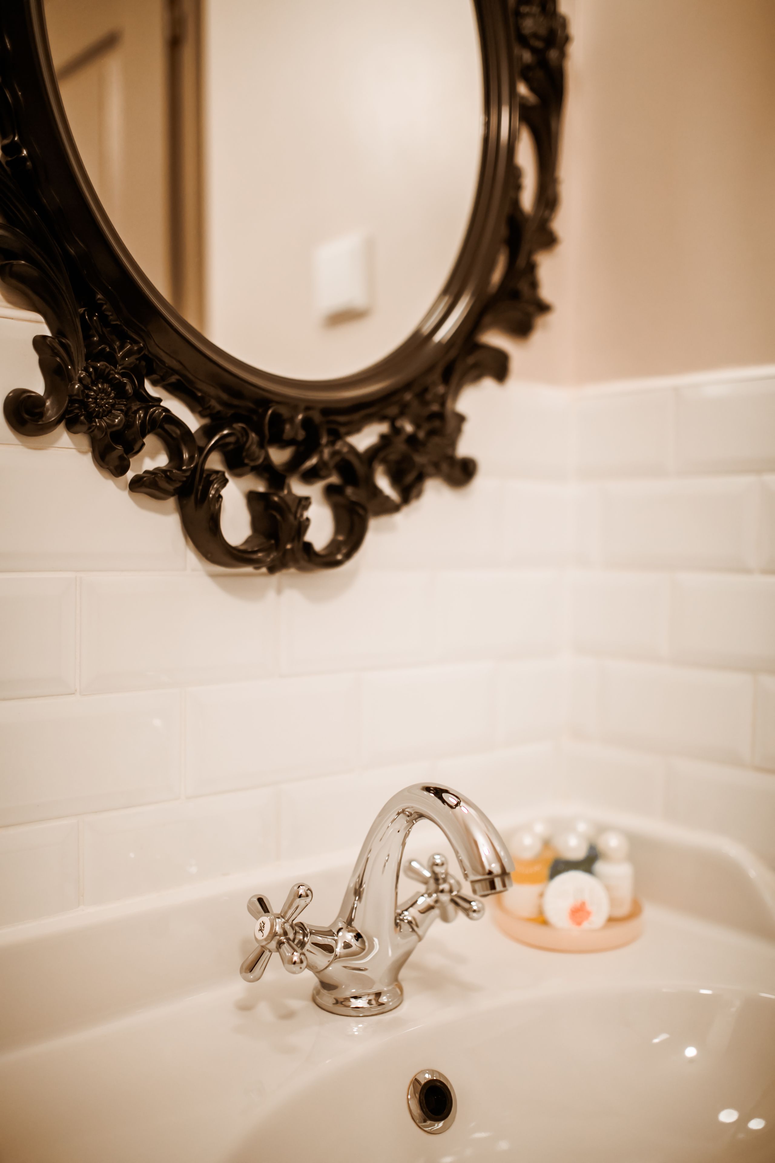 Une salle de bain avec un lavabo blanc, un miroir noir à motifs et un mur recouvert de carreaux blancs.