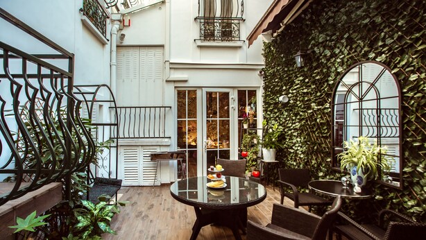 A cozy courtyard with a round glass table, wicker chairs, and potted plants. - La Maison Gobert Paris Hotel Particulier (Paris)