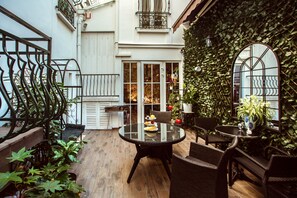 Un patio acogedor con una mesa redonda de vidrio, sillas de mimbre y plantas en macetas.
