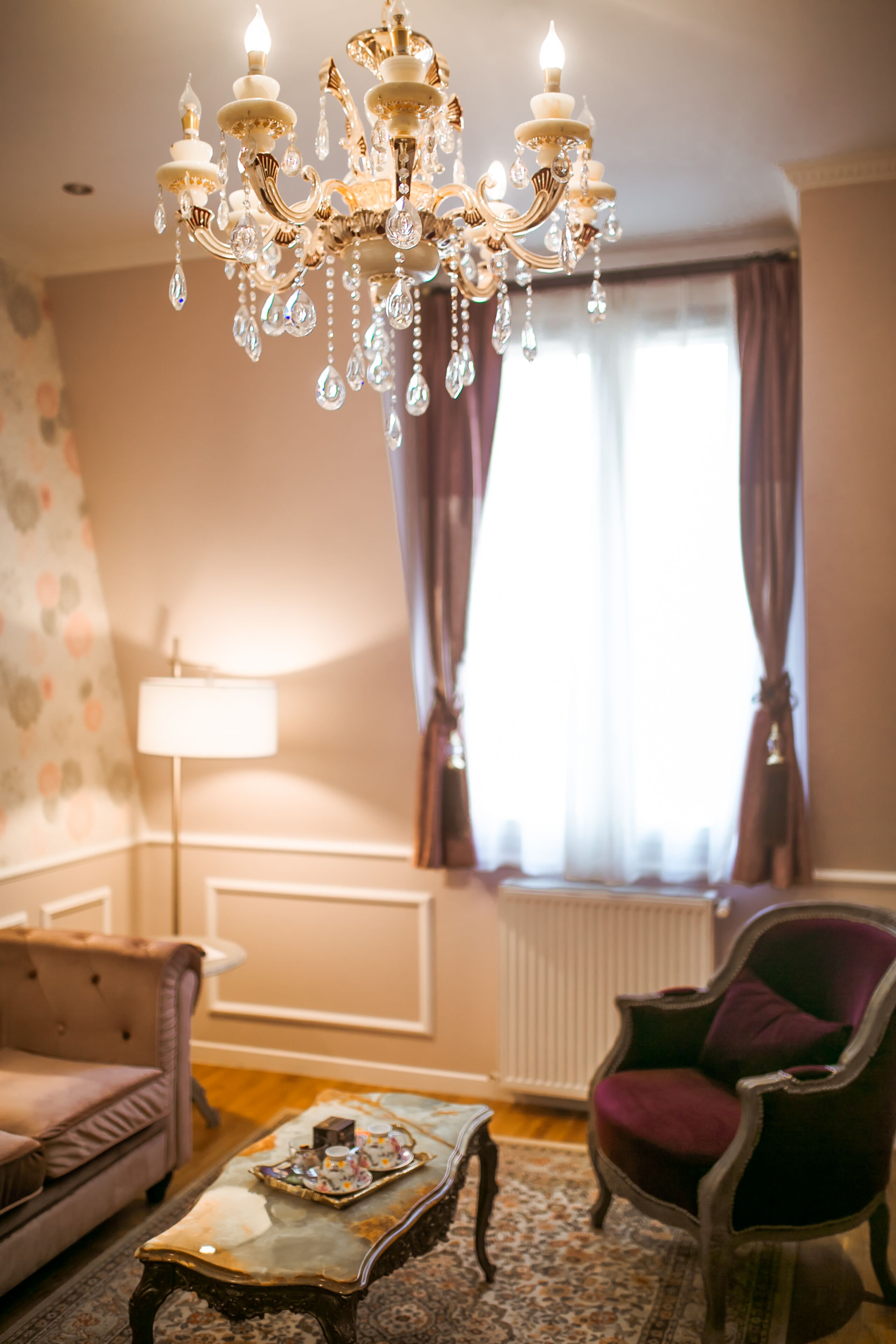Un salon avec un lustre, un canapé, un fauteuil, une lampe et un radiateur.