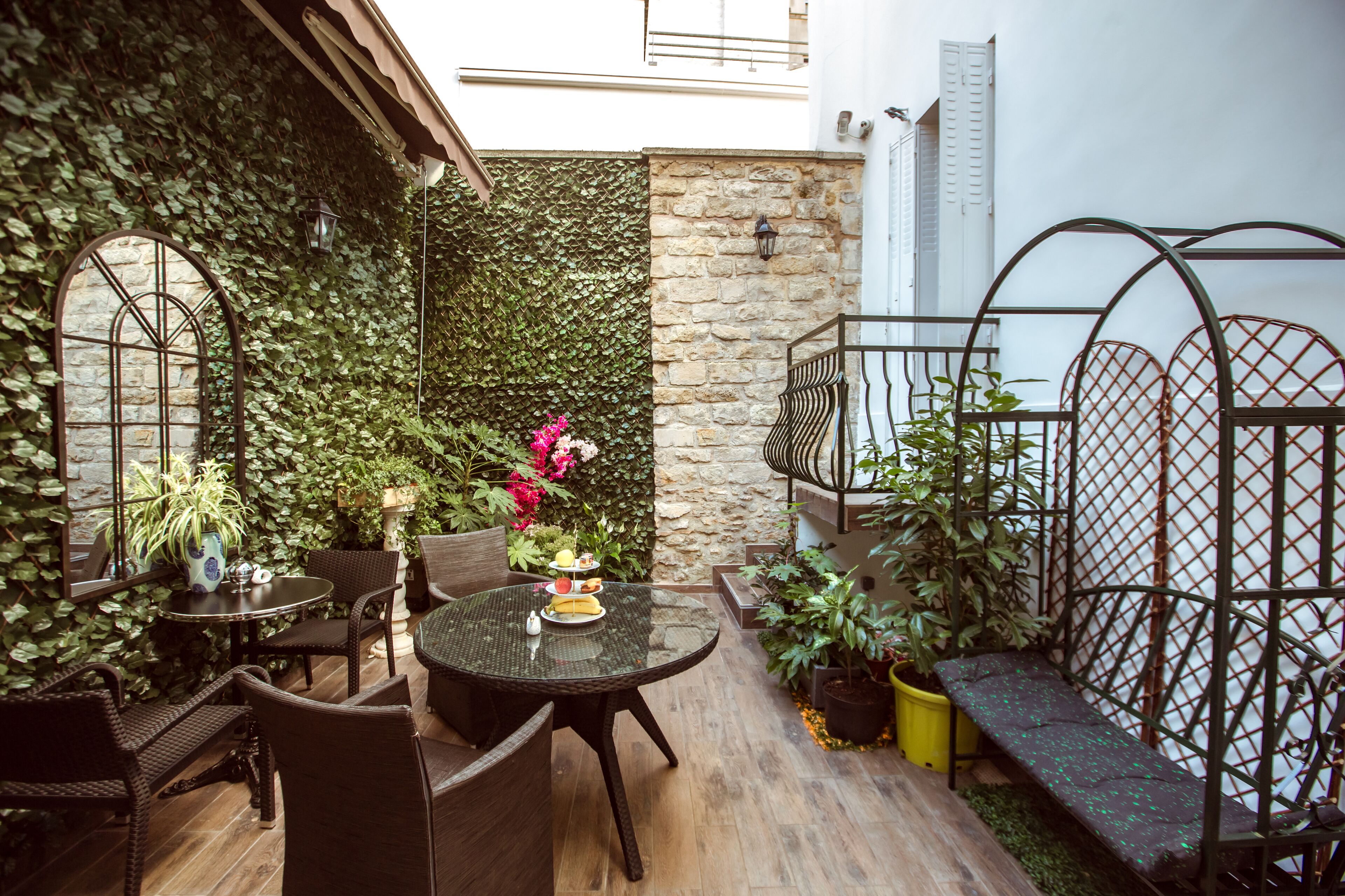 Un patio exterior acogedor con muebles de mimbre, un muro de piedra y abundante vegetación.