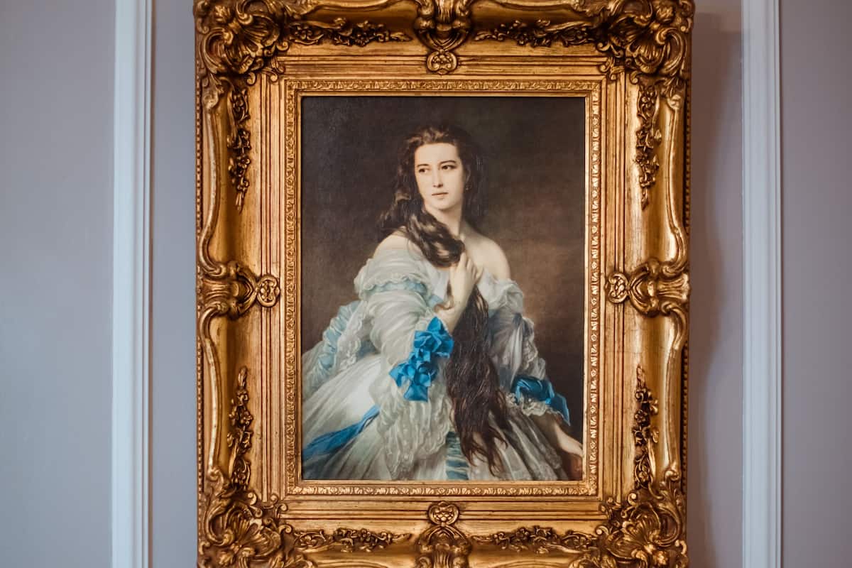 A framed portrait with an ornate gold frame, mounted on a wall with a white baseboard.