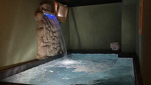 A hot tub with a waterfall feature, surrounded by stone walls and a wooden bench. - Hotel Pezzotti (Pellizzano)