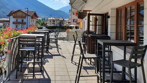 An outdoor terrace with tables and chairs, a wooden ceiling, and a mountain view in the background. - Hotel Pezzotti (Pellizzano)