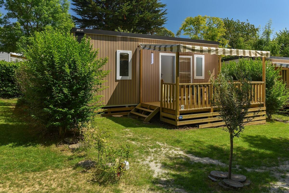 Een houten vakantiehuisje met een terras, een klein portaaltje en een raam.